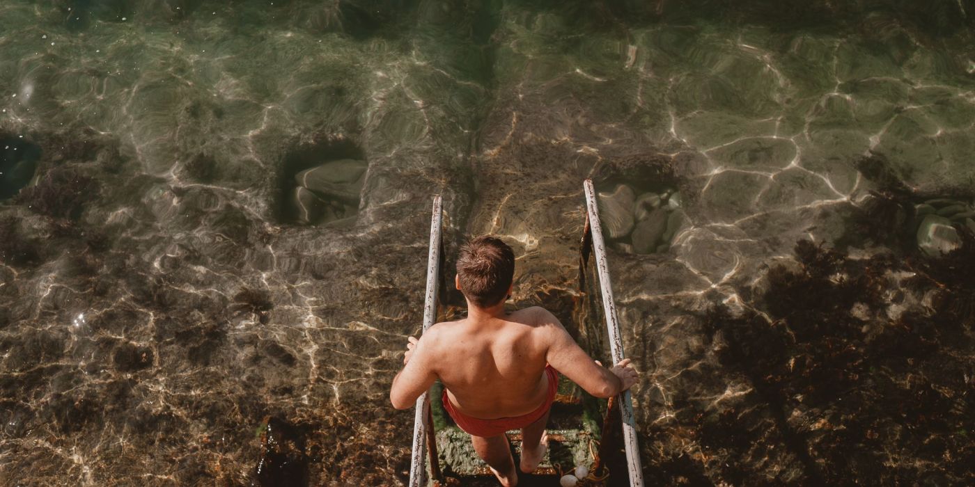Person descending a metal ladder into clear, sunlit water—capturing a refreshing, adventurous moment that reflects the laid-back Florida lifestyle near VERVE Orlando.