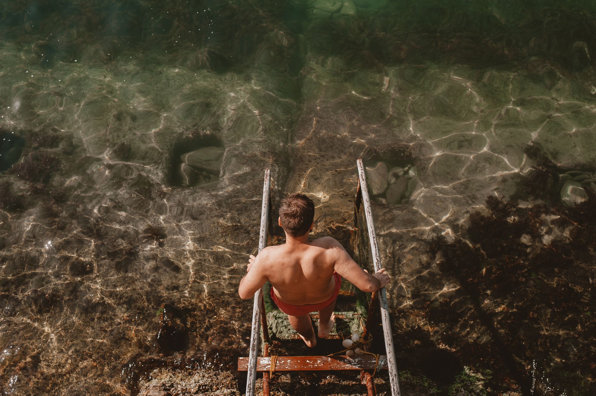Person descending a metal ladder into clear, sunlit water—capturing a refreshing, adventurous moment that reflects the laid-back Florida lifestyle near VERVE Orlando.