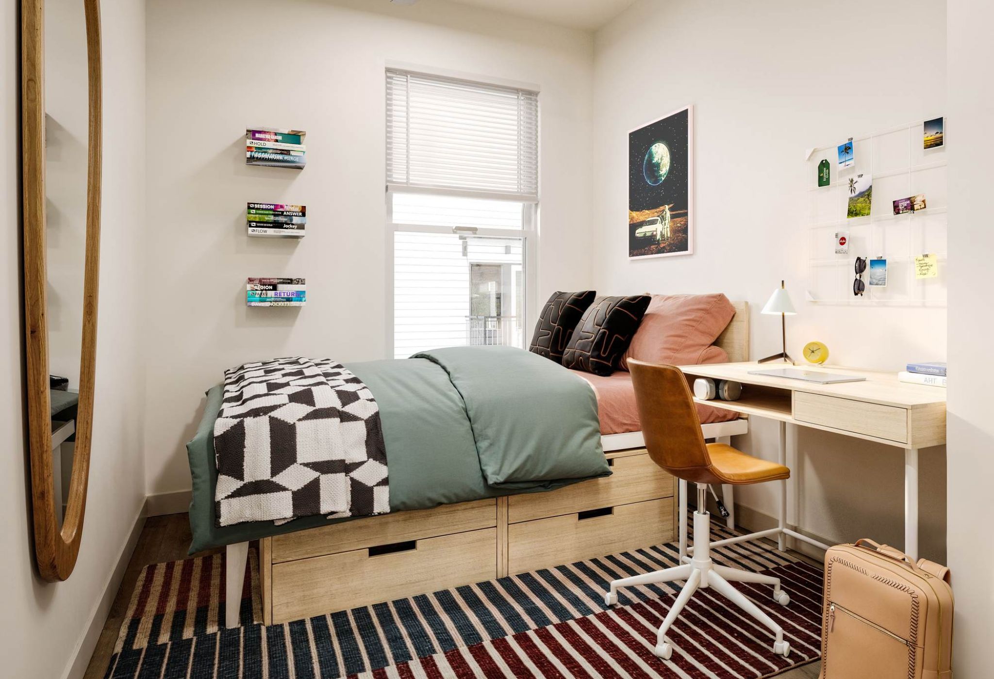 Modern student bedroom at VERVE Orlando featuring a cozy twin bed with under-bed storage, a study desk with corkboard, colorful decor, and natural light from a large window.
