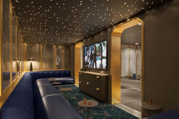 Luxe speakeasy-style lounge at VERVE Orlando featuring plush blue booth seating, a large flat-screen TV, starry ceiling lighting, and gold accents for an upscale, intimate vibe.