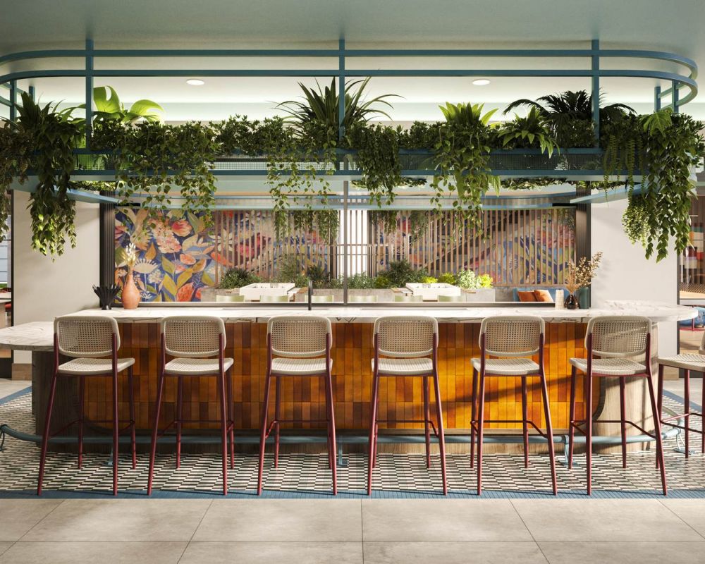 Elegante zona de bar comunitaria en VERVE Orlando con modernos asientos, exuberante vegetación, detalles artísticos en las paredes e iluminación cálida: un espacio acogedor para que los residentes se reúnan, estudien o se relajen.
