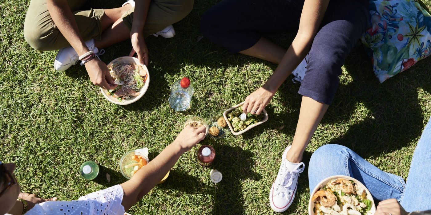 Overhead view of friends enjoying a casual picnic on the lawn with takeout bowls and drinks—capturing the sunny, social energy of life at VERVE Orlando.