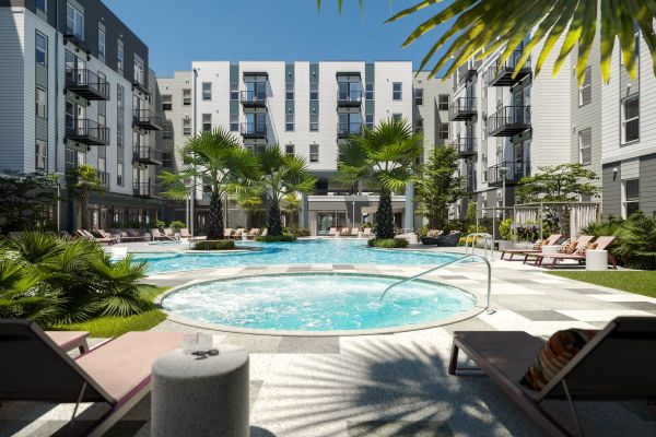 Resort-style pool courtyard at VERVE Orlando featuring a sparkling circular pool, hot tub, palm trees, lounge chairs, and surrounding modern apartment buildings—perfect for relaxing under the Florida sun.
