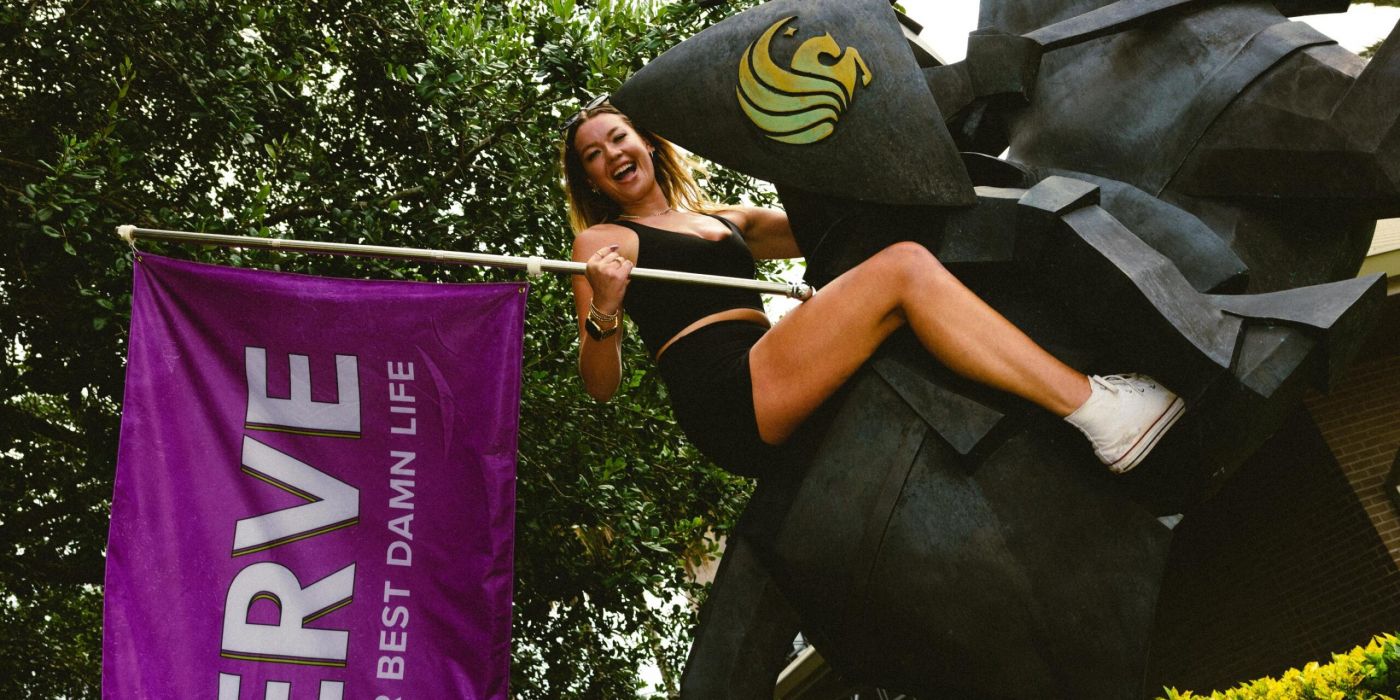 VERVE Orlando woman in black shorts poses on a horse statue next to a purple "VERVE" banner outdoors.