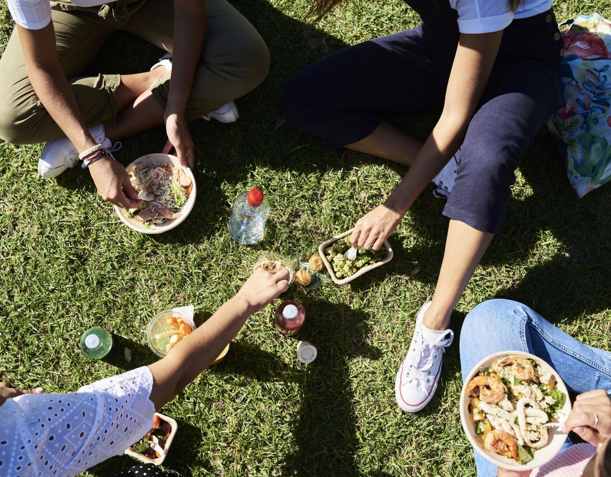 Vista aérea de amigos disfrutando de un picnic informal en el césped con comida para llevar y bebidas, capturando la energía social y soleada de la vida en VERVE Orlando.