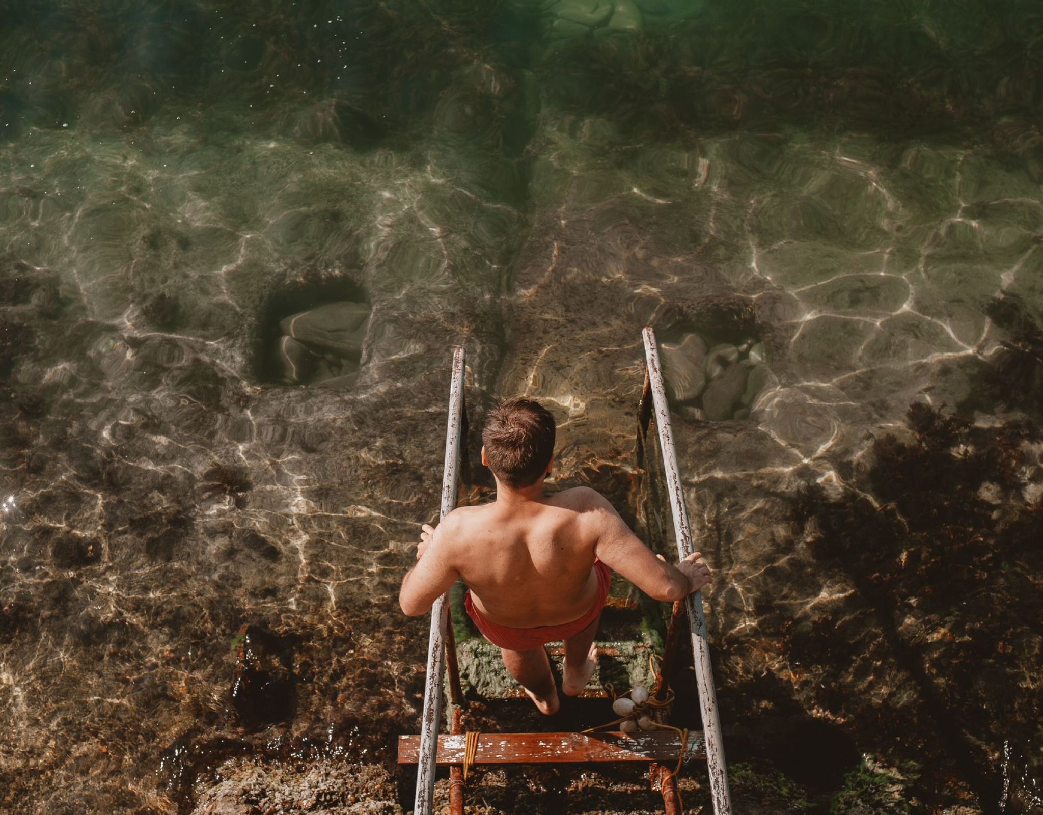Person descending a metal ladder into clear, sunlit water—capturing a refreshing, adventurous moment that reflects the laid-back Florida lifestyle near VERVE Orlando.