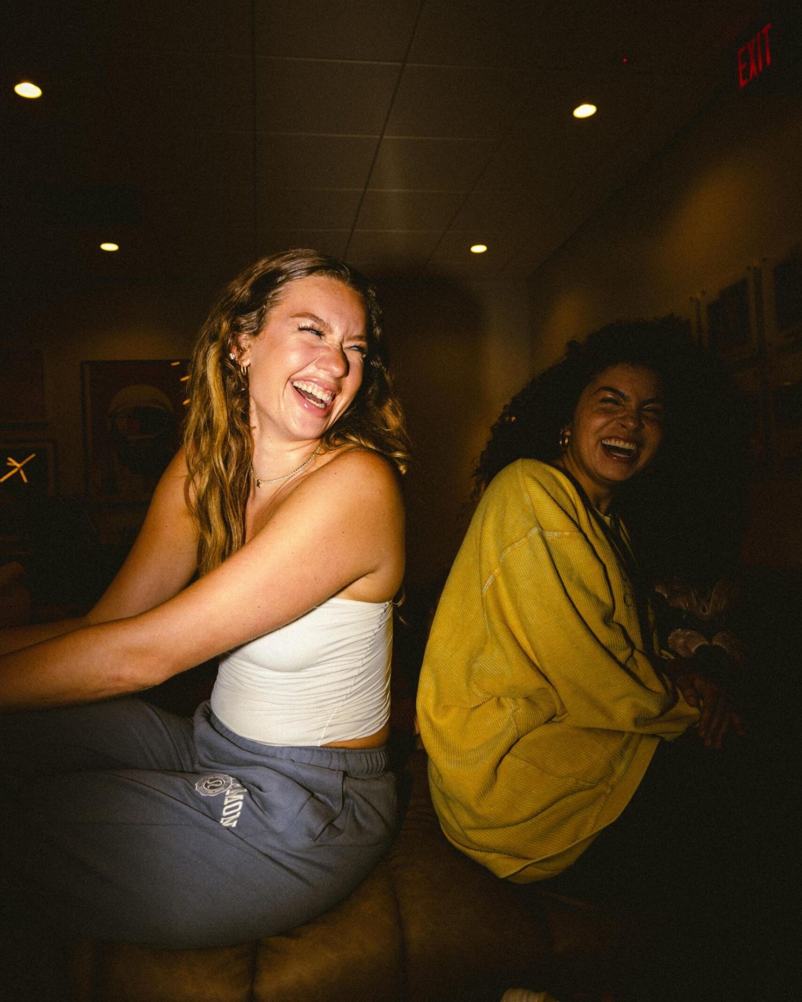 VERVE Orlando two women sitting and laughing together indoors, one in a white top and the other in a yellow sweater.