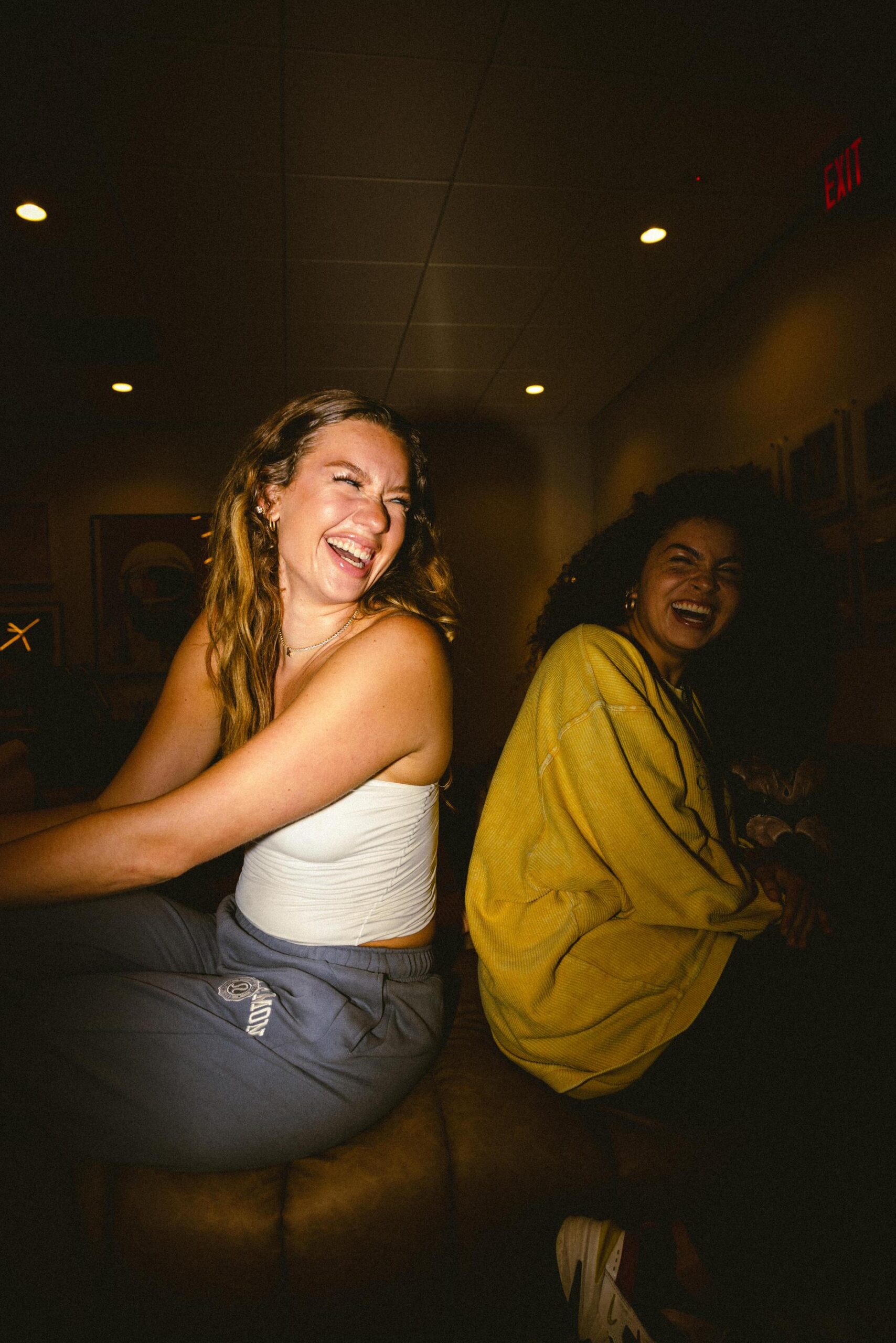 VERVE Orlando two women sitting and laughing together indoors, one in a white top and the other in a yellow sweater.